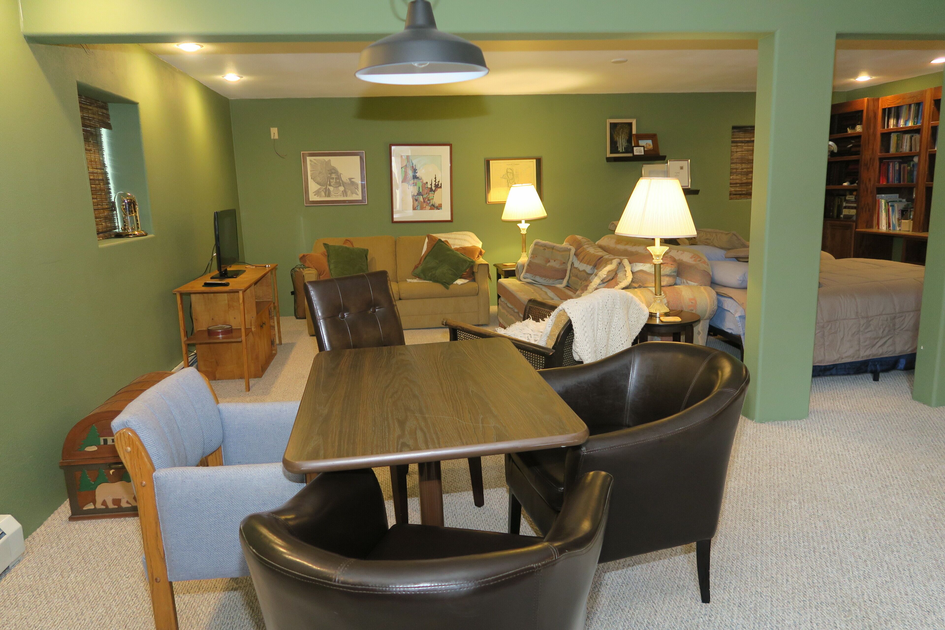 A cozy living room with a wooden dining table, leather chairs, a sofa, and a bookshelf.