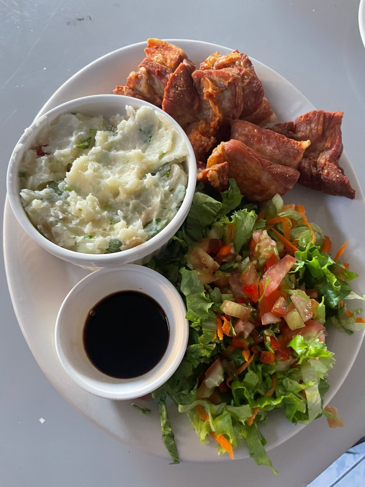 Un plato con carne asada, puré de papas, una ensalada y un recipiente pequeño con salsa.