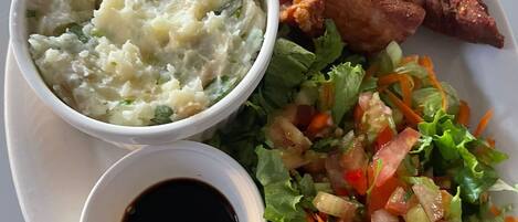 Un plato con carne asada, puré de papas, una ensalada y un recipiente pequeño con salsa.