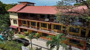 A multi-story building with a red-tiled roof, balconies, and a sign indicating it is a hotel. - Georgi, Junquillal (Veintisiete de Abril)