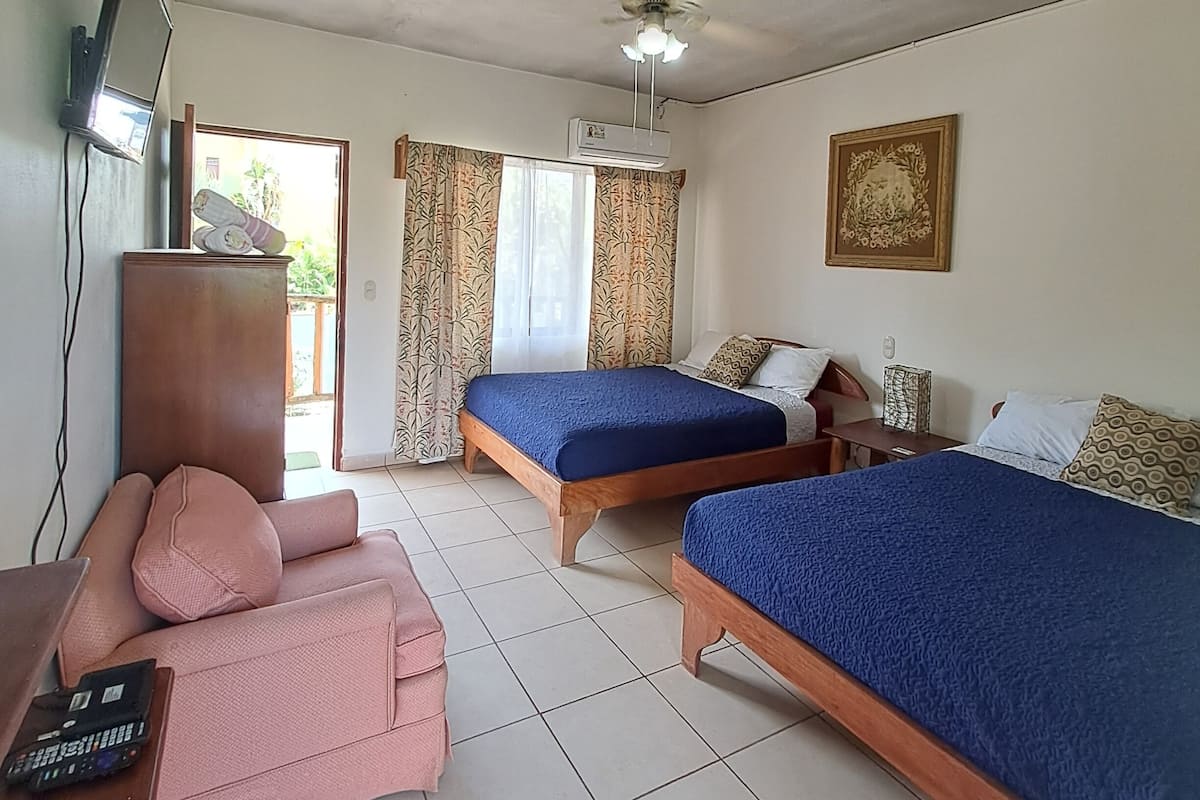 A room with two wooden beds, a television on the wall, a desk with a computer, and a pink couch.