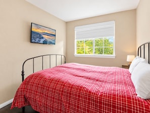 Un dormitorio con cama, ventana con vista a árboles y un cuadro en la pared.