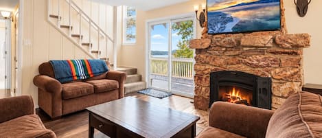 A living room with a stone fireplace, a sofa, a coffee table, and a TV mounted above the fireplace.