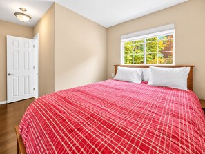 A bedroom with a bed, a window with a view of trees, and a door. - Hibernation Haven (Big Bear Lake)