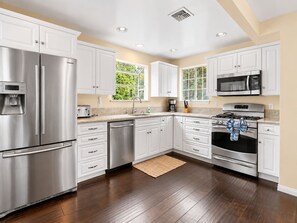 Una cocina moderna con electrodomésticos de acero inoxidable, armarios blancos y un amplio ventanal que proporciona luz natural.