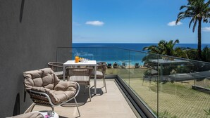 A balcony with a table and chairs, a glass railing, and a view of the ocean and palm trees. - Acqua Residence VIII – Sea View and Pool (Funchal)