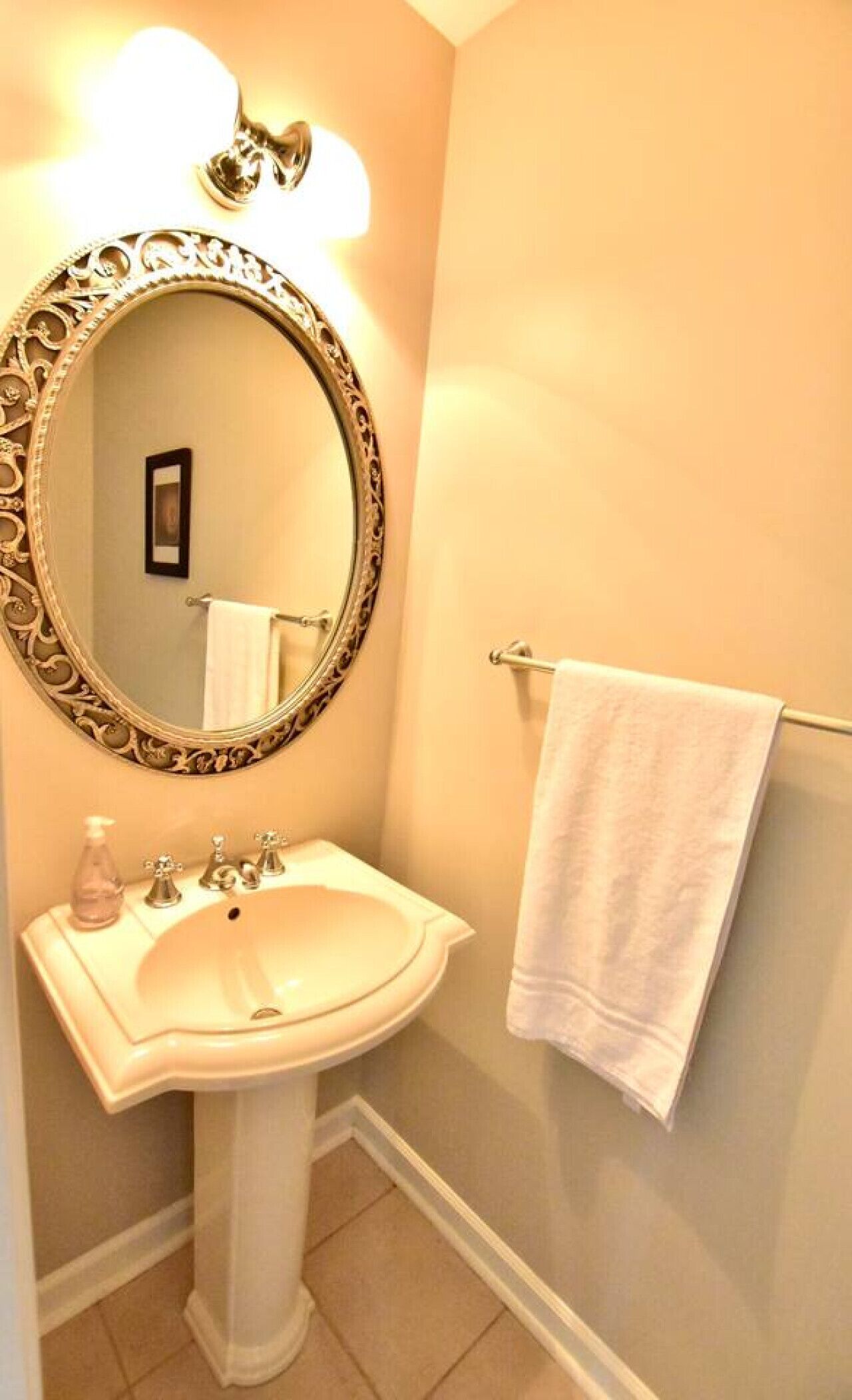 Une salle de bain avec un lavabo sur colonne, un grand miroir décoratif et un porte-serviettes sur lequel est posée une serviette blanche.