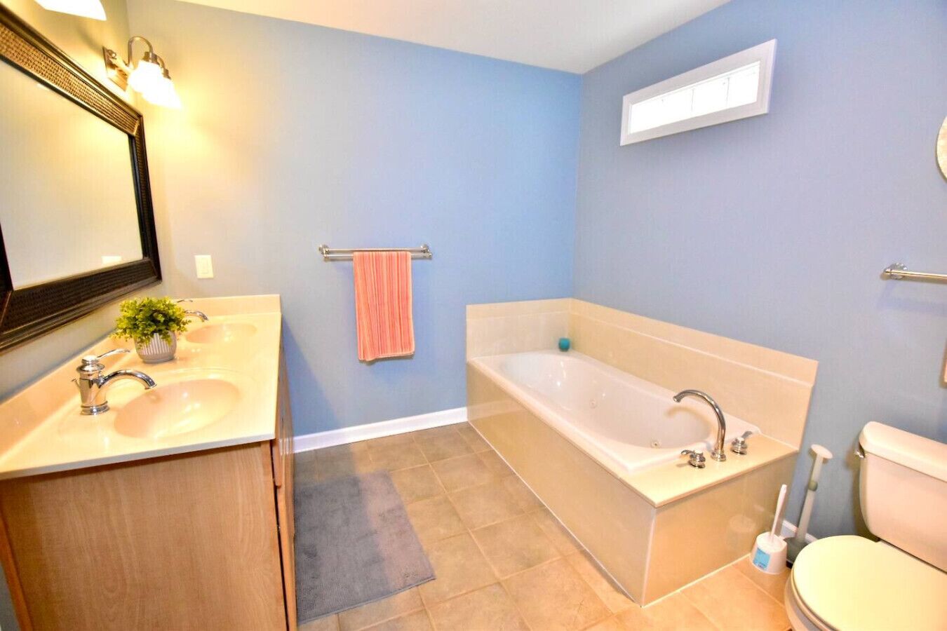 Un baño con bañera, dos lavamanos, inodoro, espejo y toallero.