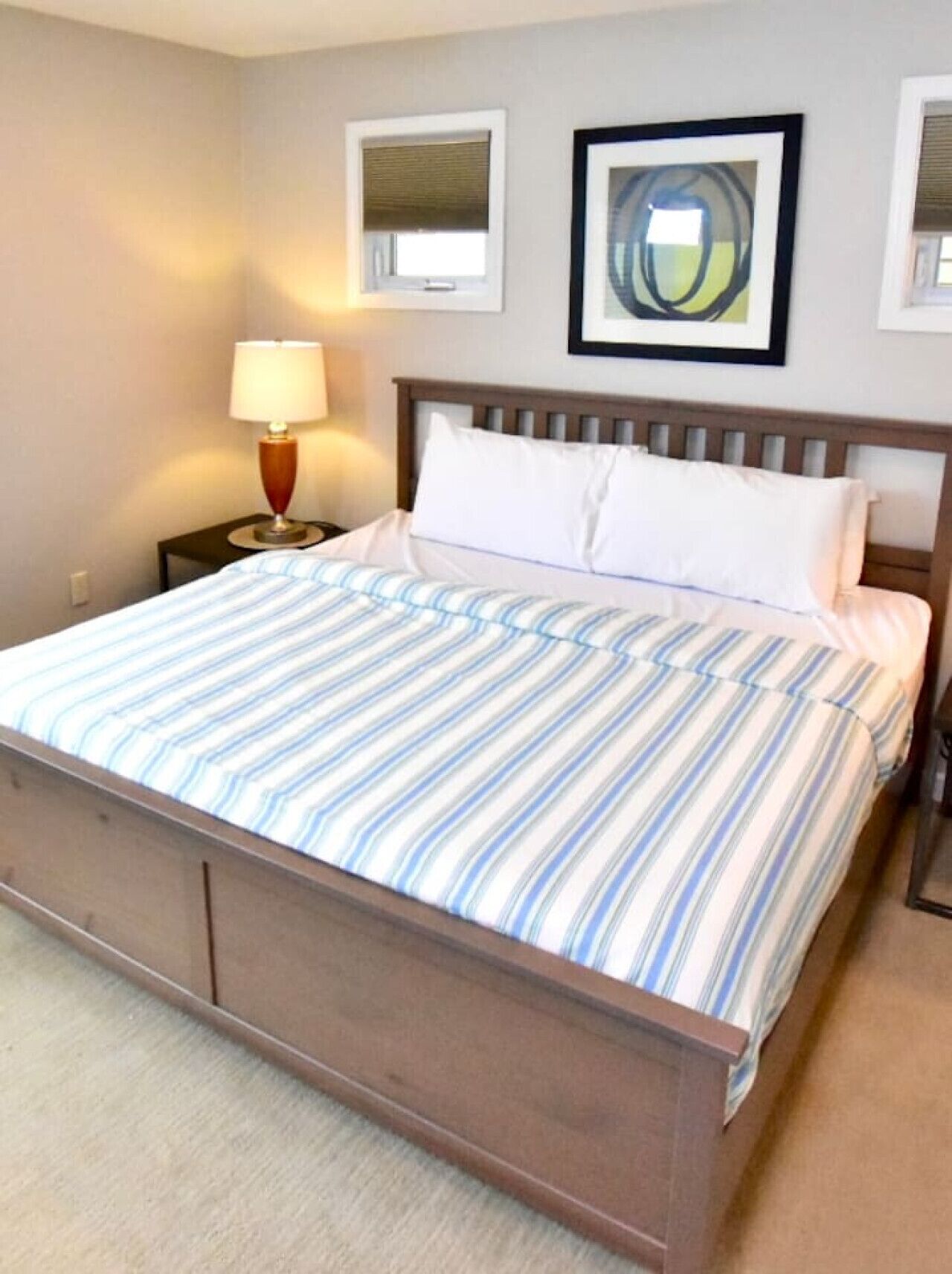 Une chambre à coucher avec un lit en bois, une literie à rayures, une table de chevet avec une lampe et deux tableaux encadrés au mur.