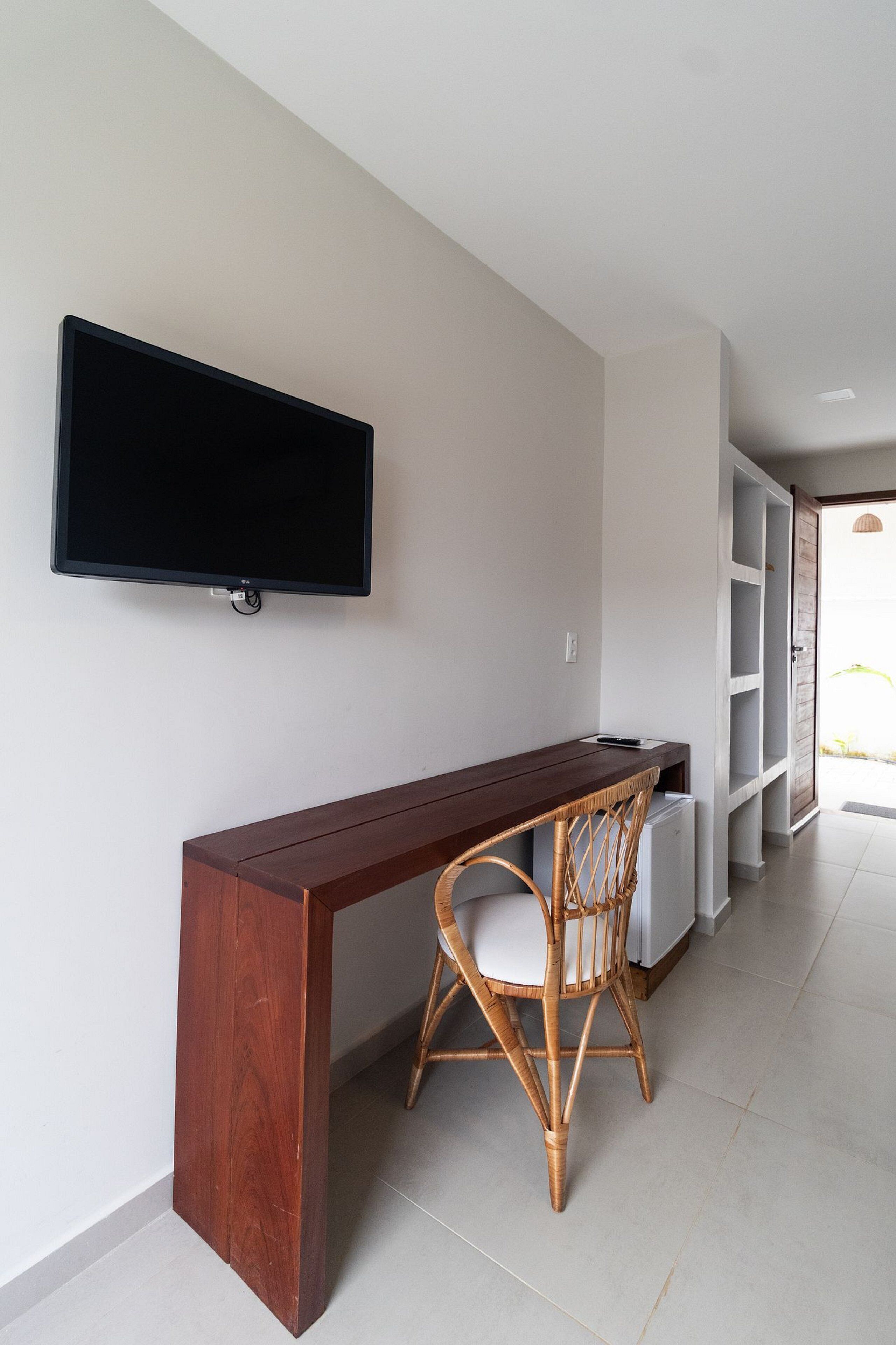 Quarto moderno com escrivaninha de madeira, cadeira de vime, TV de tela plana na parede e prateleiras embutidas.
