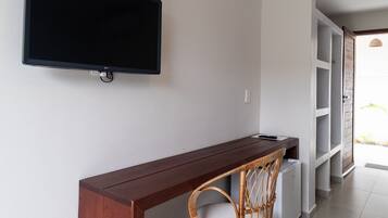 Quarto moderno com escrivaninha de madeira, cadeira de vime, TV de tela plana na parede e prateleiras embutidas.