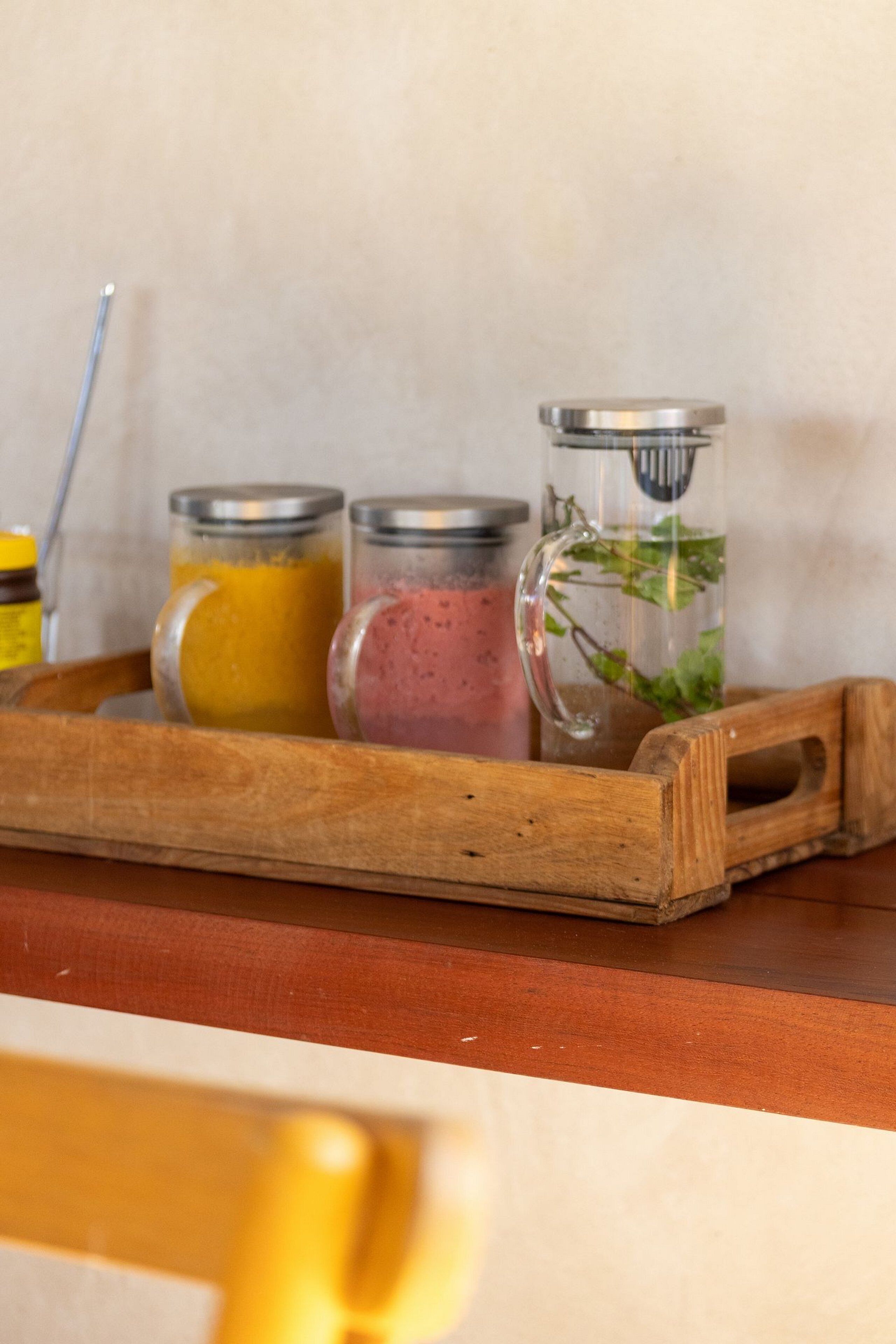 A wooden tray with three glass containers holding different colored liquids, placed on a wooden surface.