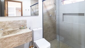 Un baño moderno con cabina de ducha de vidrio, encimera de mármol y un inodoro.