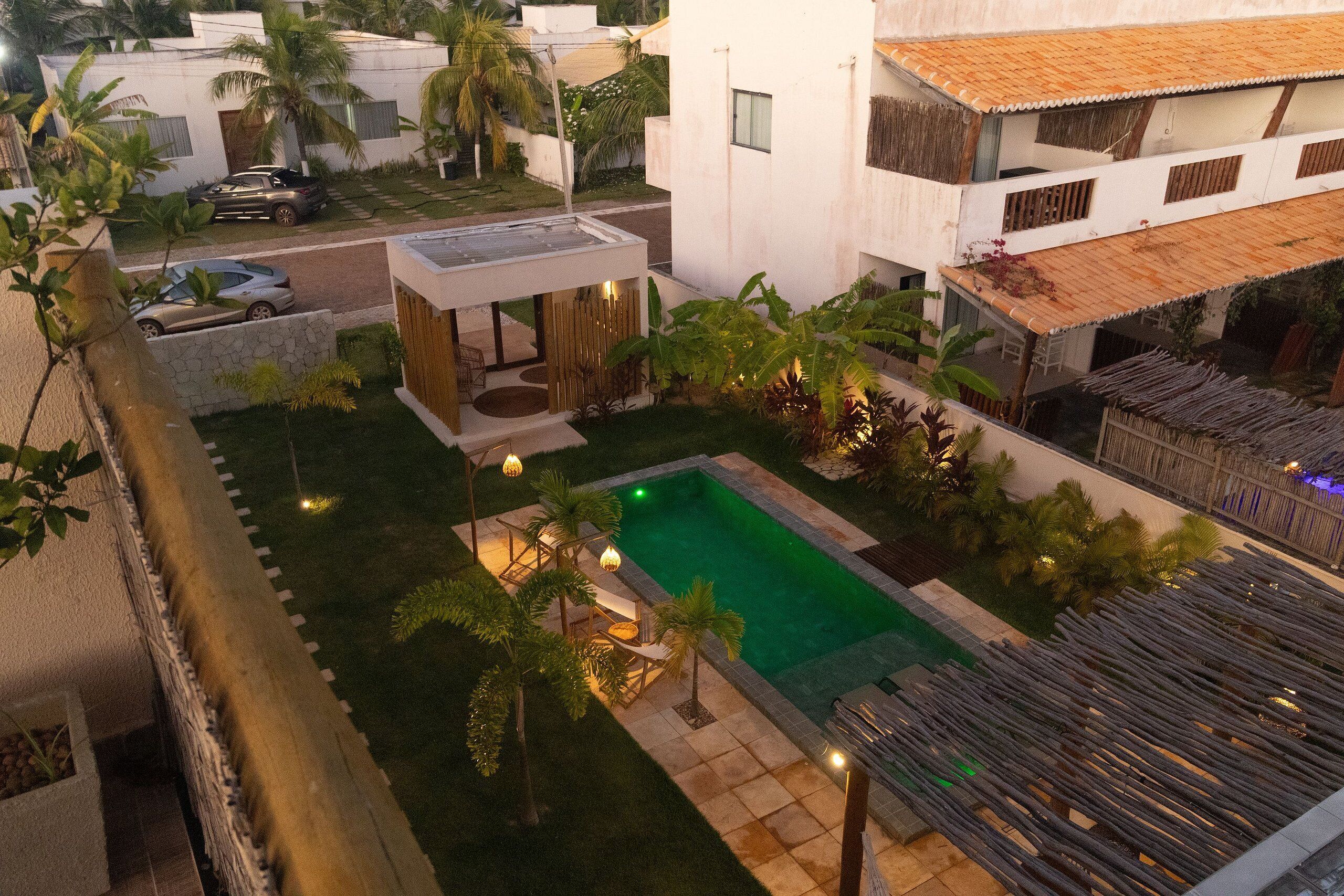 A residential area with a swimming pool, a covered patio, and a street with parked cars.