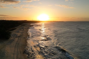 A beach with a sunset over the ocean, a sandy shoreline, and a distant horizon. - Pousada Oasis dos Ventos (Touros)