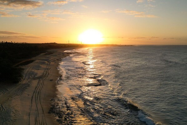 Una playa con un atardecer sobre el océano, una orilla arenosa y un horizonte lejano.