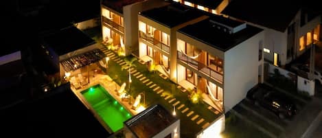 A modern multi-story building with a swimming pool, outdoor lighting, and a carport.