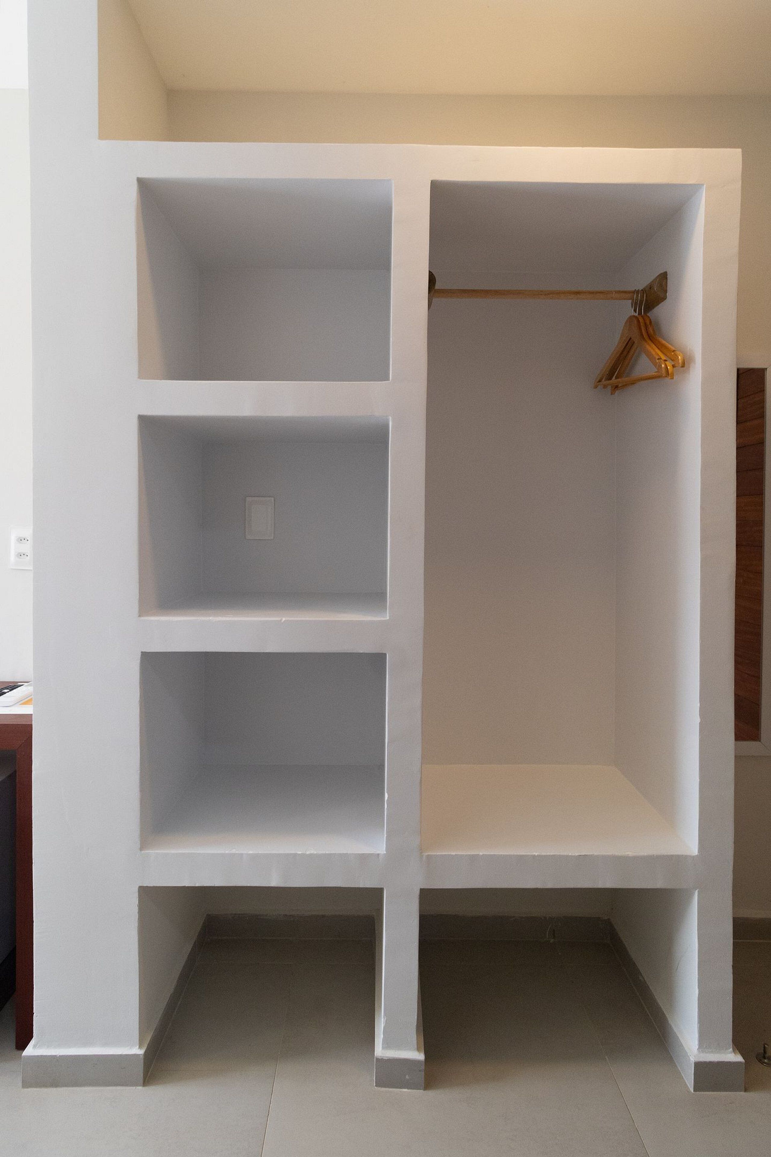 Un armario blanco con varios estantes y una barra para colgar ropa.