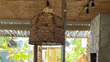 A buffet setup with various food items and utensils, a hanging woven light fixture, and a view of the outdoors.