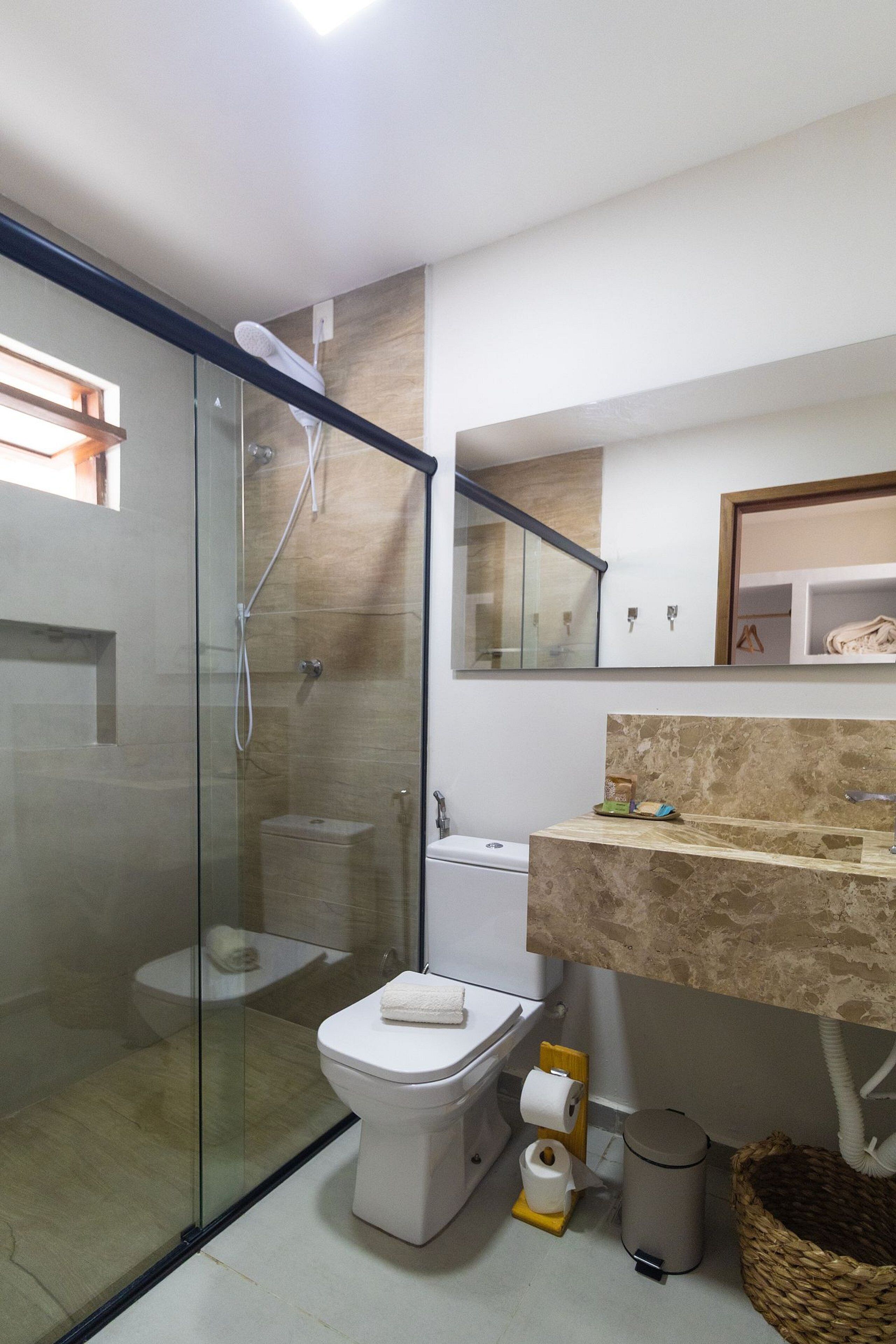 A modern bathroom with a glass-enclosed shower, a toilet, and a sink with a marble countertop.