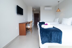 Habitación de hotel con cama, escritorio, silla, televisor y lámpara colgante.