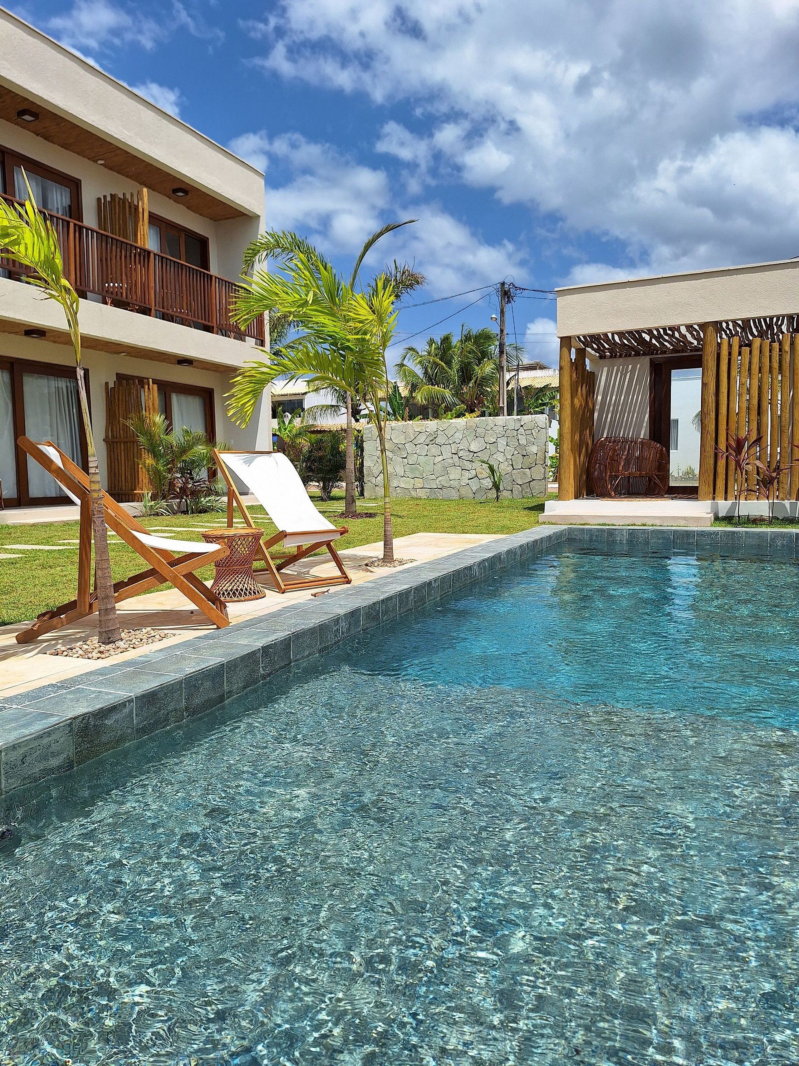 A clear swimming pool with lounge chairs, a stone wall, and a building with a balcony.