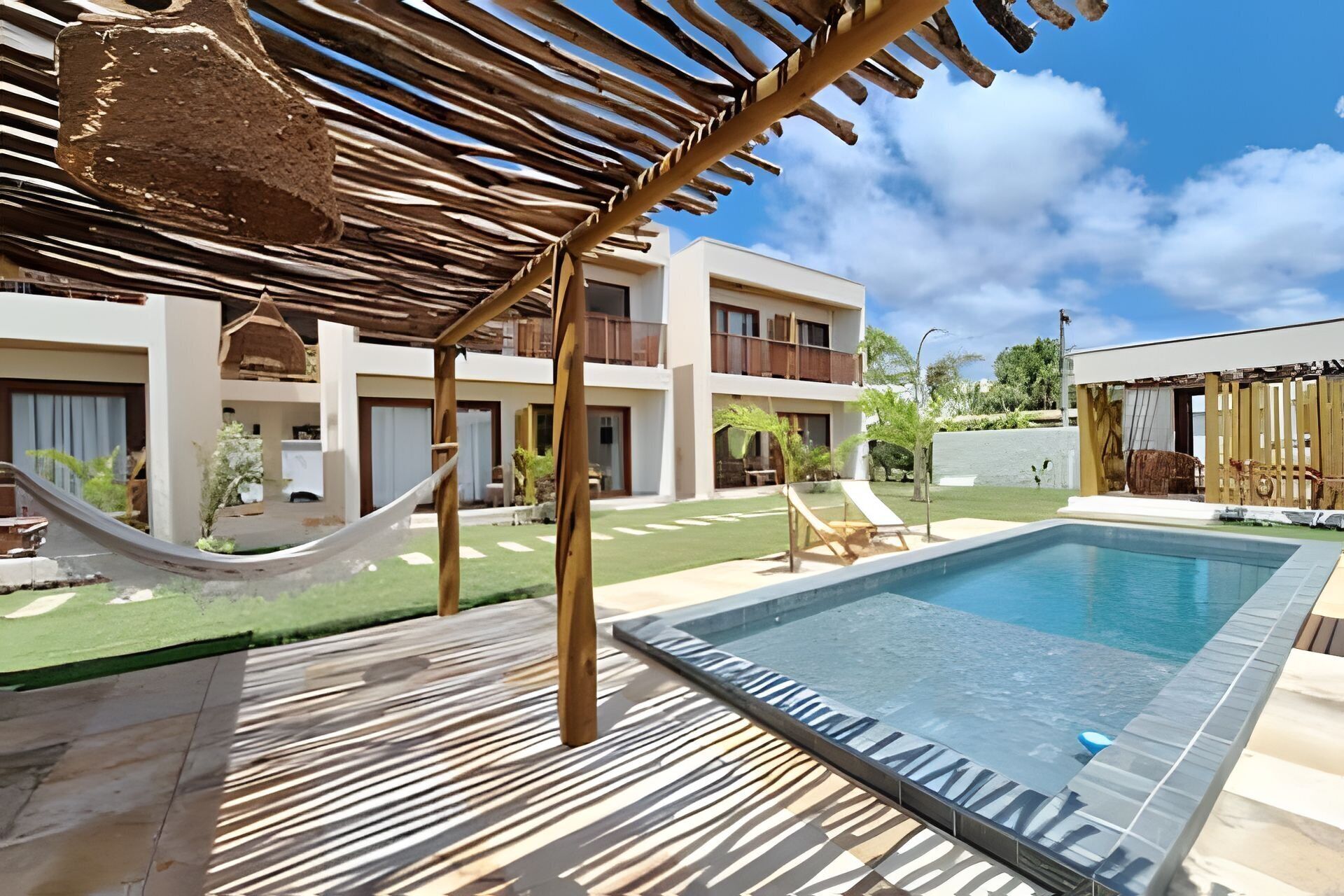A pool area with a hammock, lounge chairs, and a building with balconies.