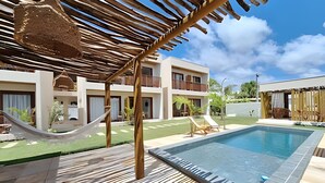 A pool area with a hammock, lounge chairs, and a building with balconies. - Pousada Oasis dos Ventos (Touros)
