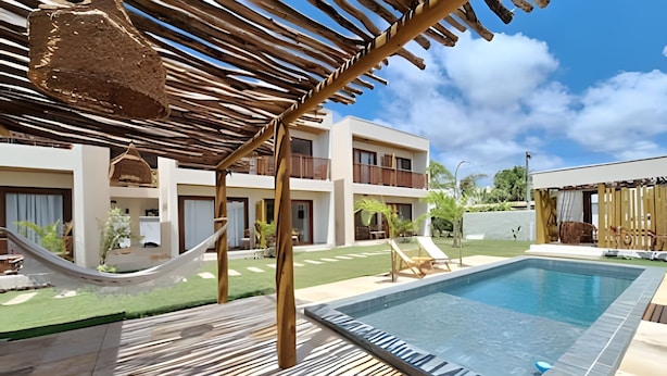 Zona de piscina con una hamaca, sillas de descanso y un edificio con balcones.