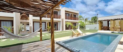 A pool area with a hammock, lounge chairs, and a building with balconies.