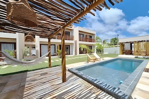 A pool area with a hammock, lounge chairs, and a building with balconies. - Pousada Oasis dos Ventos (Touros)