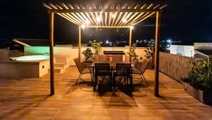 Un patio al aire libre con una pérgola, una mesa con sillas, un jacuzzi y plantas en macetas.
