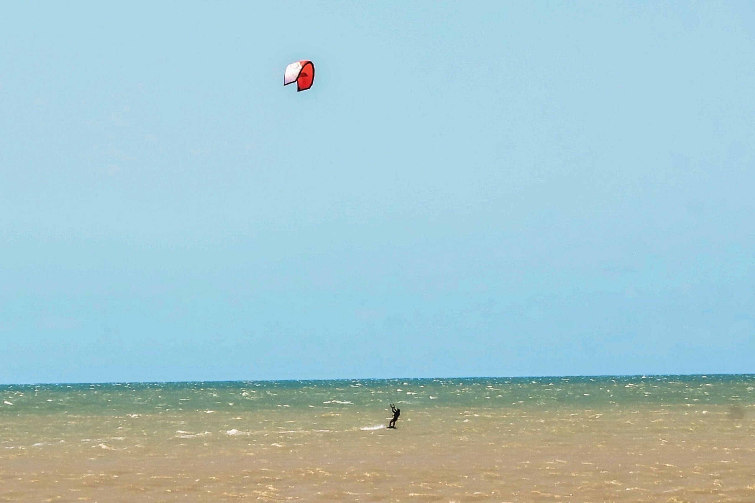 Ein Strand mit einer Person, die Kitesurfen geht.