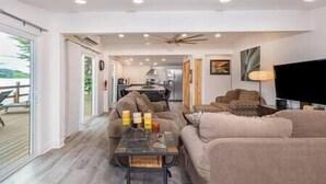 A spacious living room with a large sofa set, a coffee table, and a flat-screen TV. There is a sliding glass door leading to an outdoor area with a deck. - Island House on Lake Moraine (Madison)