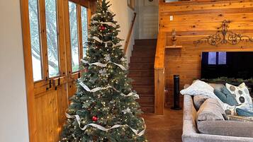 A cozy living area with a wooden staircase, a Christmas tree, and a comfortable couch.