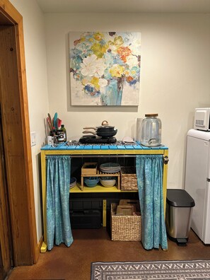 Una cocina con una mesa azul, un microondas y un cubo de basura.