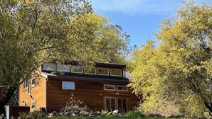 A wooden cabin with a front porch, a small deck, and a signboard. - Rustic Studio Getaway in the California Gold Country - Pet Friendly (Penn Valley)
