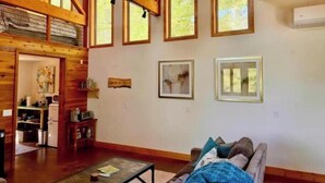 A cozy living room with wooden beams, a fireplace, and a dining area with a kitchen in the background. - Rustic Studio Getaway in the California Gold Country - Pet Friendly (Penn Valley)