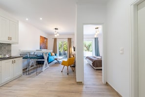 Une cuisine moderne avec des meubles blancs, un coin repas avec un canapé bleu et une chaise jaune, et un salon avec un canapé et une fenêtre.