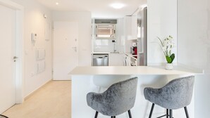 Una cocina moderna con armarios blancos, un refrigerador de acero inoxidable y una pequeña isla con dos sillas grises.