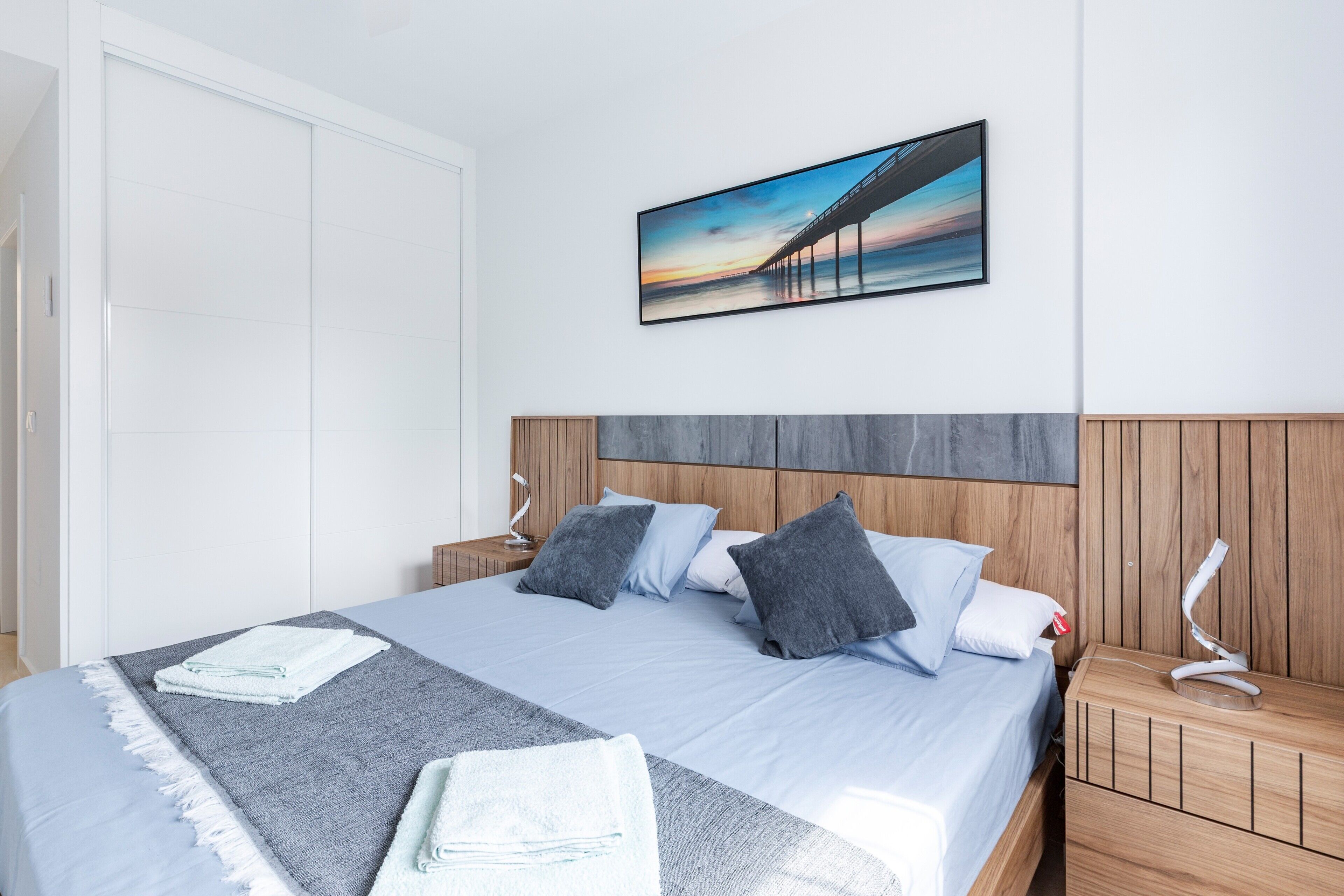 A neatly made bed with pillows, a bedside lamp, and a picture on the wall.