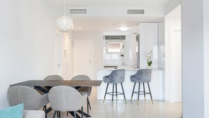 Una cocina moderna con comedor, sillas tapizadas en gris y una lámpara colgante.