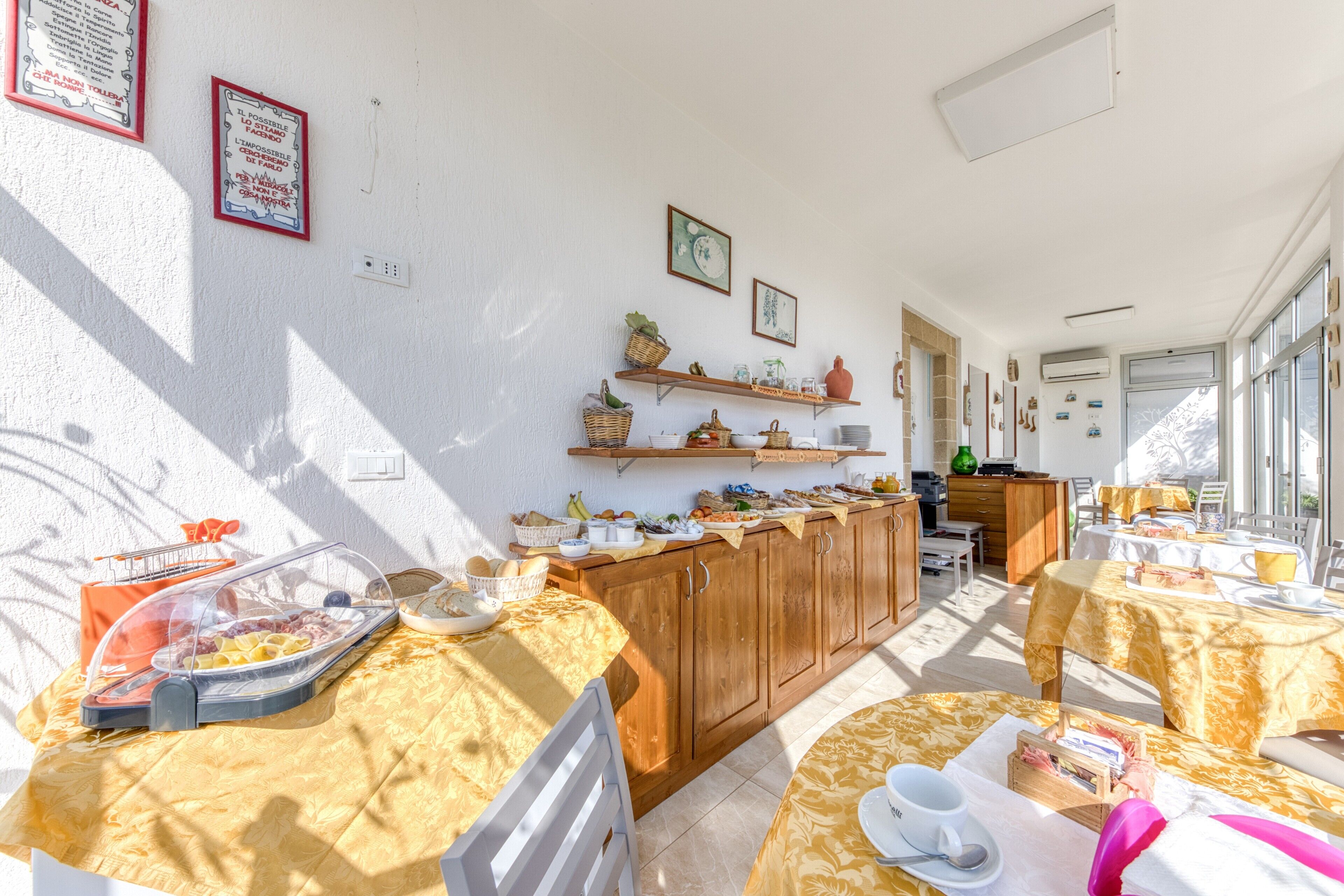 A sunlit kitchen with wooden cabinets, a buffet setup, and a dining area with tables and chairs.