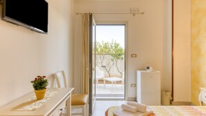 Une chambre d’hôtel comprenant un lit, un bureau, une chaise, une télévision, une petite table avec un pot de plante et une vue sur l’extérieur.