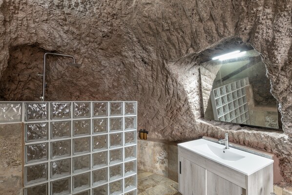 A bathroom with a stone wall, a glass shower enclosure, a sink, and a mirror.