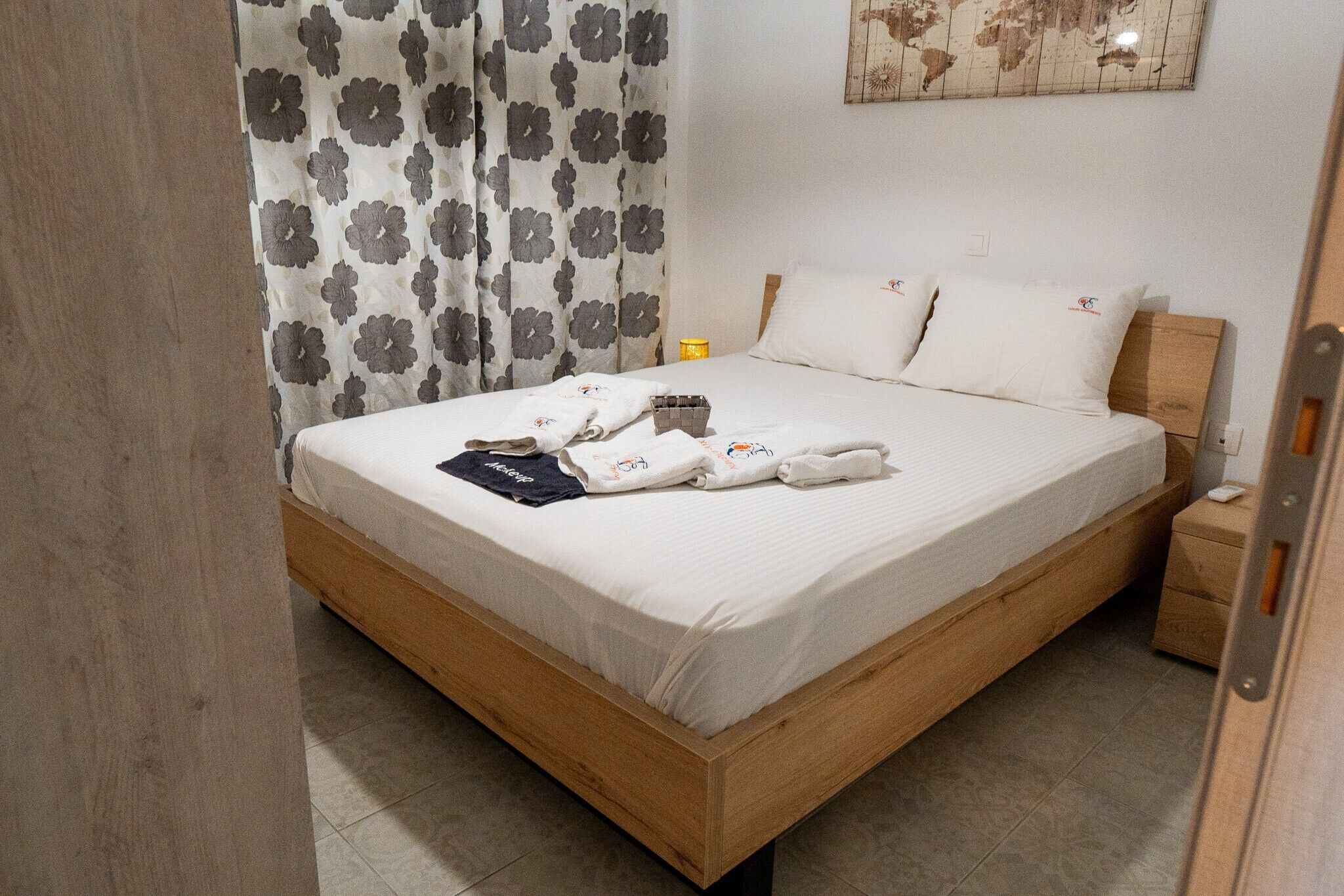 A bed with a wooden frame, white bedding, and a floral curtain.