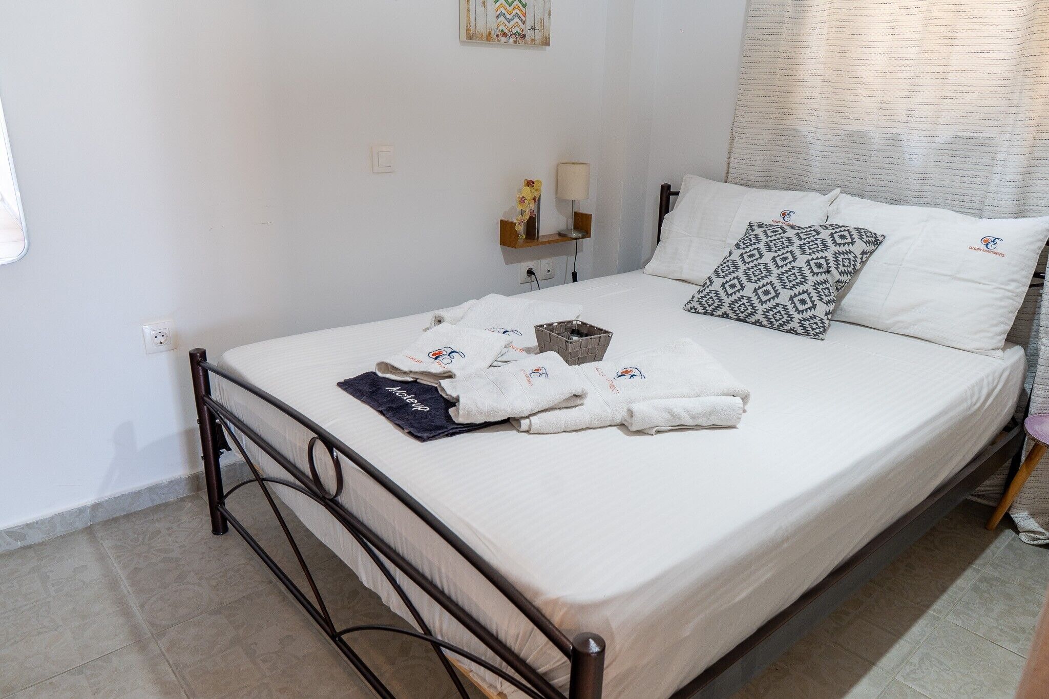 Un lit avec du linge de lit blanc, un cadre en métal et une table de chevet avec une lampe et un petit objet décoratif.