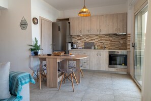 A modern kitchen with wooden cabinets, a built-in oven, and a dining area with a round table and chairs. - Apartment 'Evagelia Luxury  3' with Shared Pool, Wi-Fi and Air Conditioning (?e??ada)