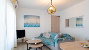 A modern living room with a sofa, round tables, a flat-screen TV, a painting of sailboats, a mirror, and a wooden door. - Apartment 'Evagelia Luxury  3' with Shared Pool, Wi-Fi and Air Conditioning (?e??ada)