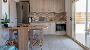 A modern kitchen with wooden cabinets, a built-in oven, a refrigerator, and a dining area with a clear chair and a table. - Apartment 'Evagelia Luxury  3' with Shared Pool, Wi-Fi and Air Conditioning (?e??ada)